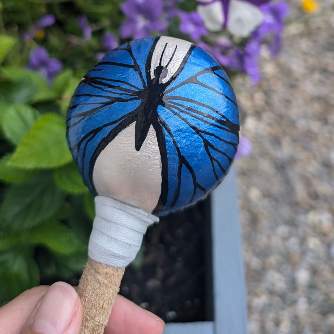Handheld rattle with blue butterfly design held against a natural background
