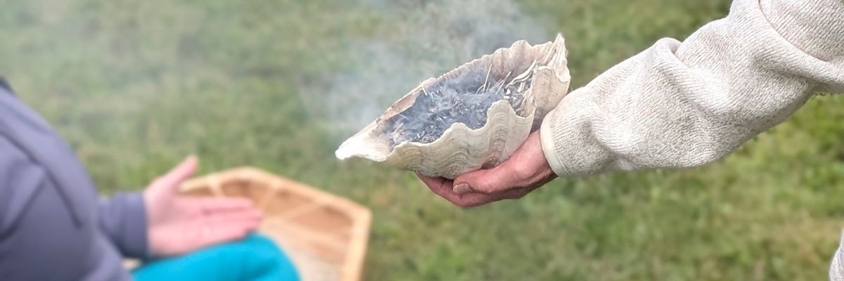 A person holding out a large shell filled with smoking herbs as an offering