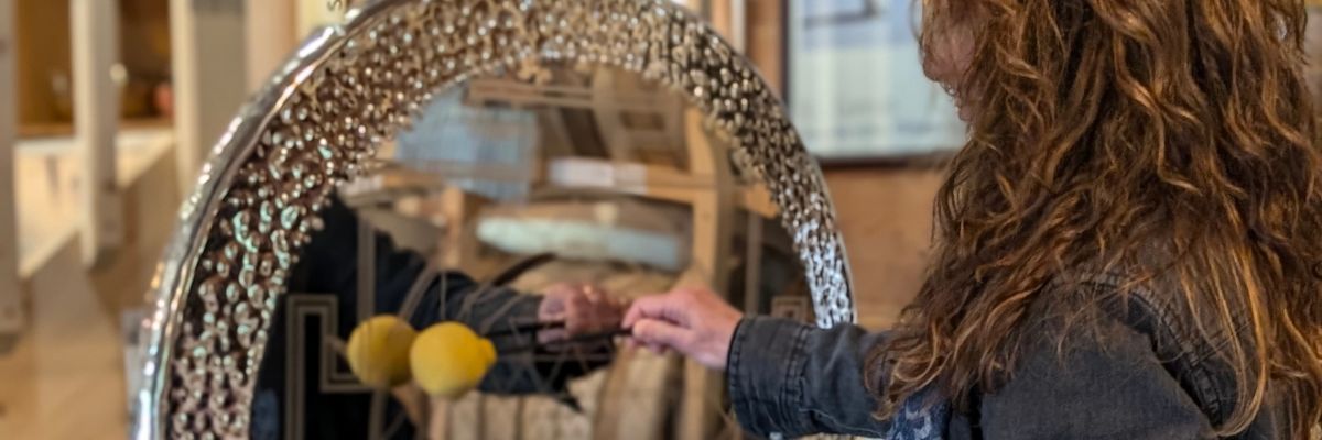 A person with long hair striking a large polished silver gong