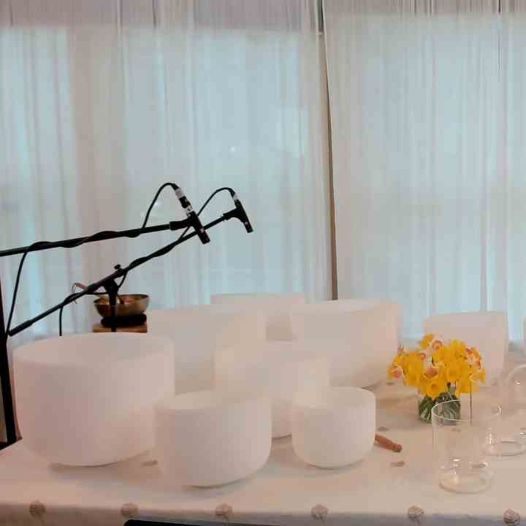 multiple crystal singing bowls on a table with two microphones on stands