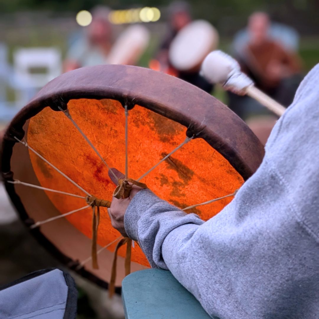 Person playing a large hide drum with a blurred background