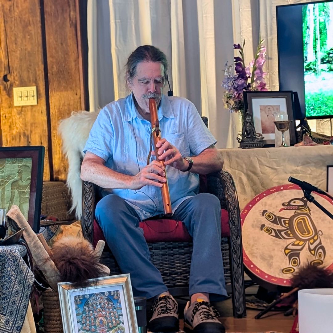Zacciah Blackburn playing a flute during a retreat with a drum and framed pictures.