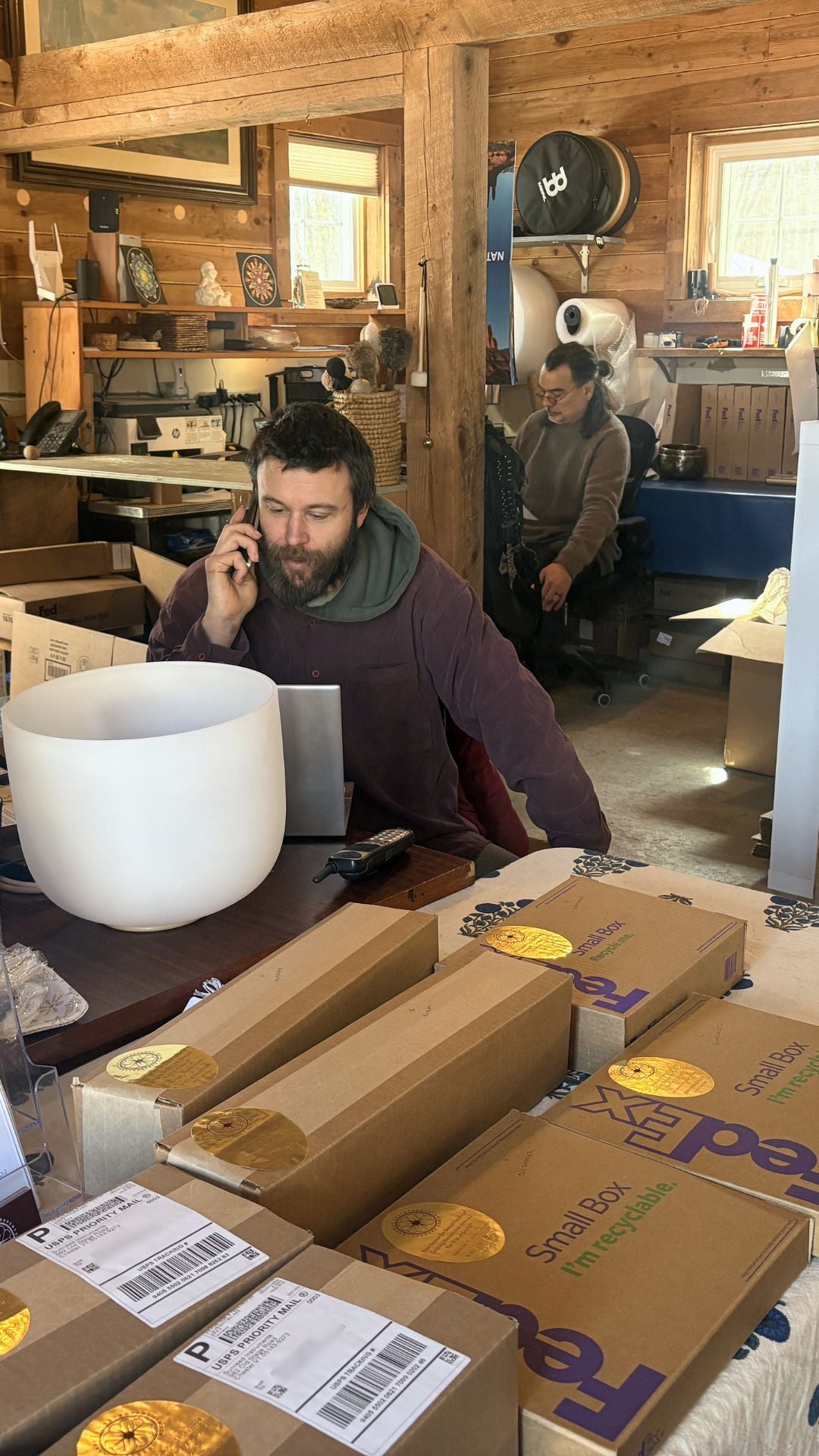 Man on phone in Sunreed shop with shipping boxes and crystal signing bowl around