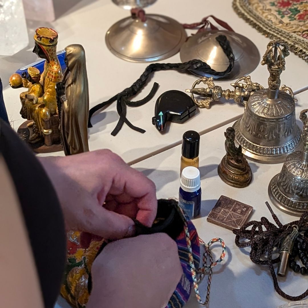 Hand holding a small pouch with various bells and altar items on a table