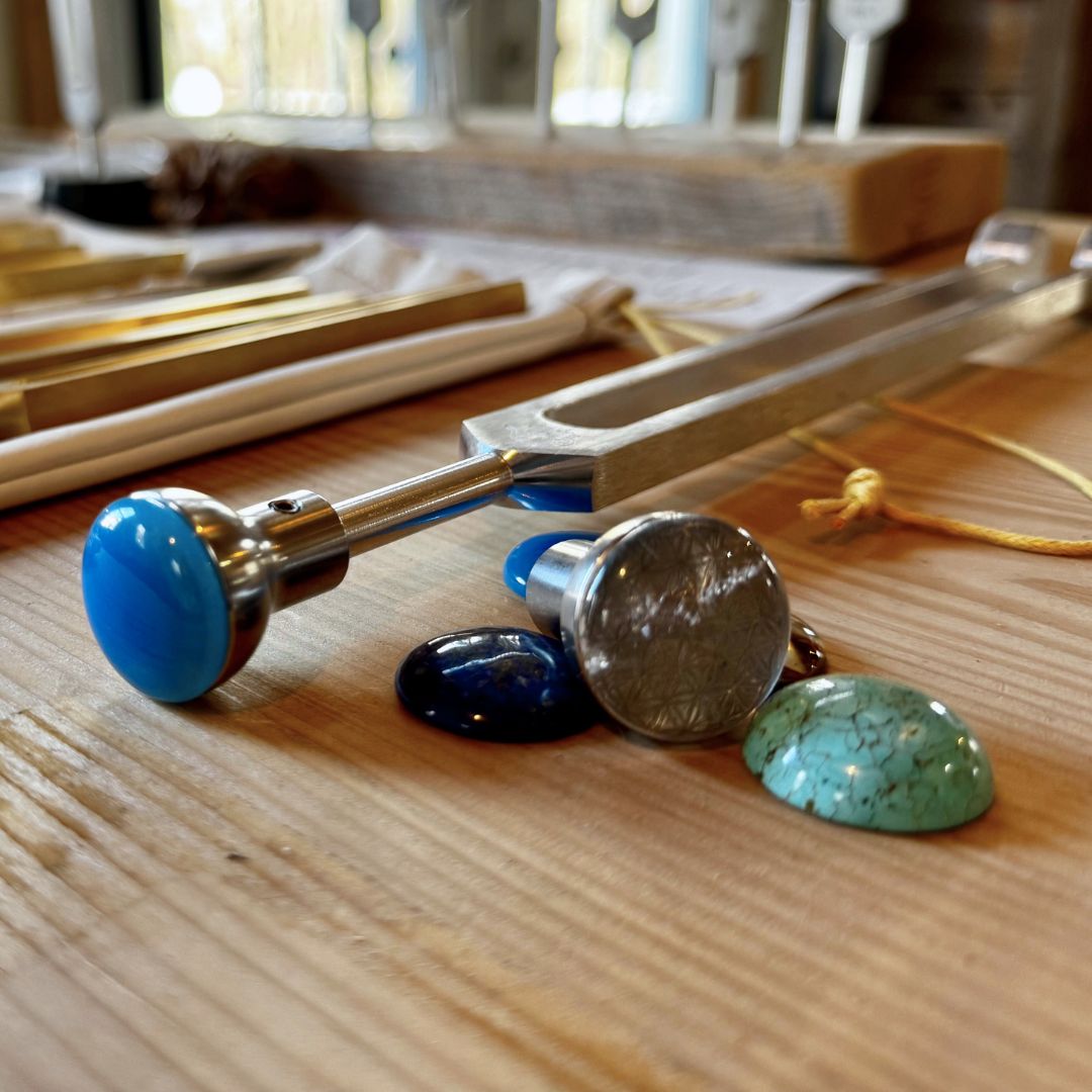 blue and green crystal attenuators besides a tuning fork on a wooden surface