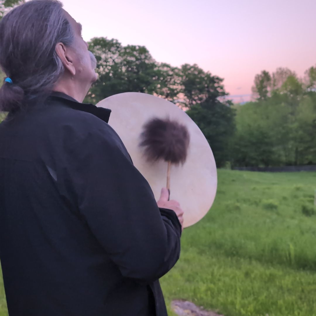 Zacciah Blackburn playing a natural hide drum in an outdoor setting